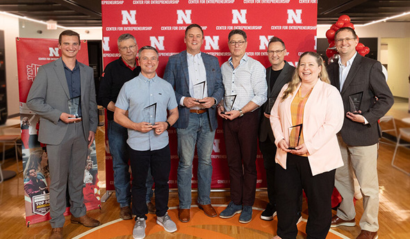 Group of people holding awards, standing on a wood floor, with a red "N" branded backdrop.